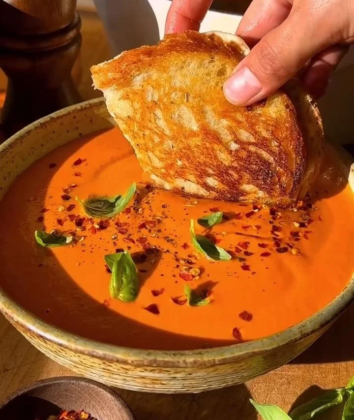Bowl of creamy tomato soup served with a grilled cheese sandwich on the side