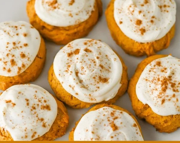 Cream cheese frosted pumpkin cookies on a platter, decorated for fall