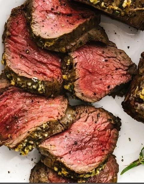 Juicy and tender beef tenderloin roast on a cutting board with herbs.