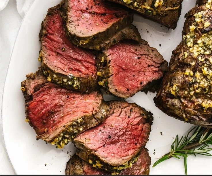 Juicy and tender beef tenderloin roast on a cutting board with herbs.