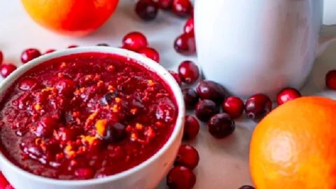 Homemade cranberry sauce in a bowl garnished with fresh cranberries and herbs.
