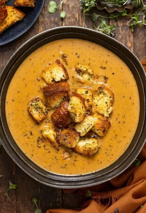 Creamy roasted apple and pumpkin soup served in a bowl, garnished with herbs.