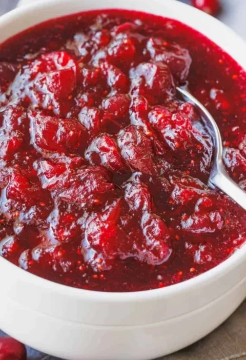 Homemade cranberry sauce in a glass bowl, garnished with fresh cranberries.