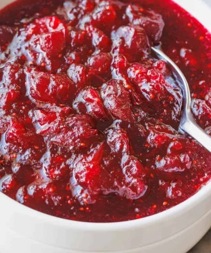 Homemade cranberry sauce in a glass bowl, garnished with fresh cranberries.