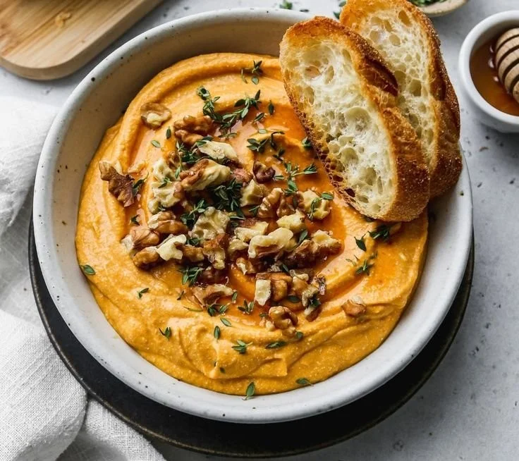 Pumpkin Whipped Feta Dip served in a bowl with herbs and crackers