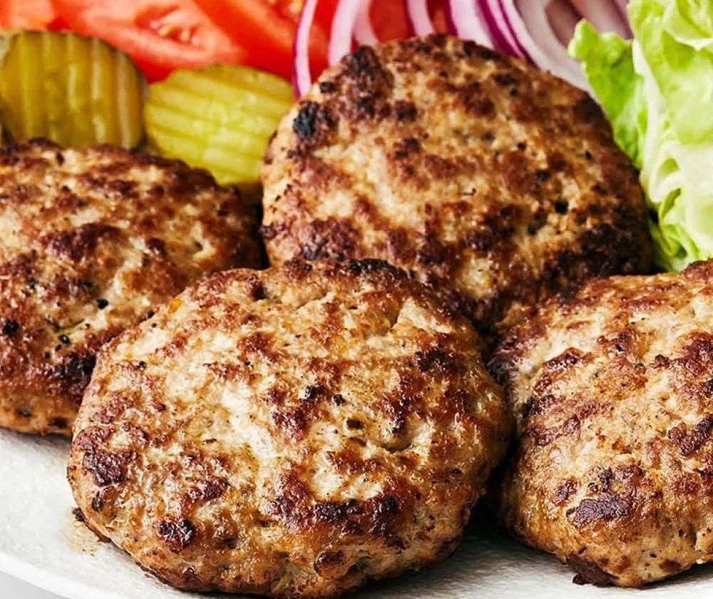 Juicy turkey burger patties on a grill with fresh ingredients