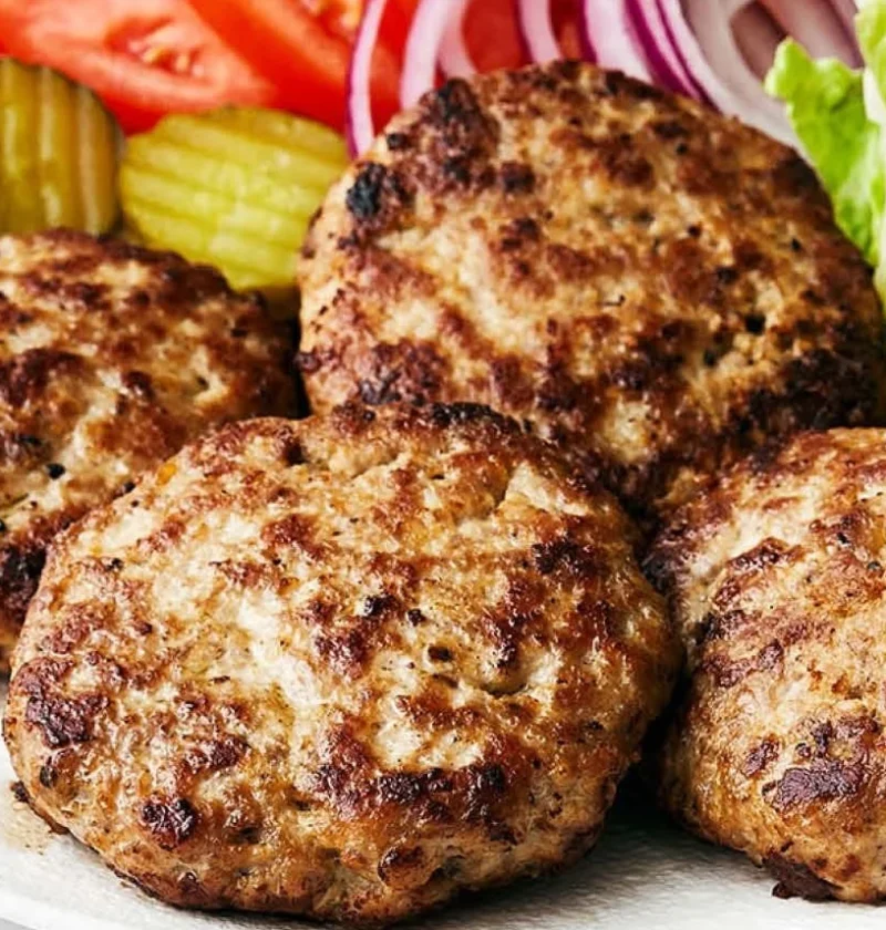 Juicy turkey burger patties on a grill with fresh ingredients